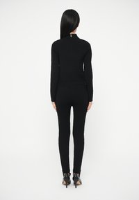 Mustast kudumist kaheosaline komplekt, mis koosneb vormistatud kõrge kaelusega pika varrukaga topist ja sobivatest vormistatud pükstest, kombineeritud mustade kontsadega.