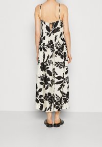 Maxiklänning i svart och vitt blommönster, tillverkad av lättviktsmaterial, har justerbara spaghetti-remmar och en avslöjande ryggdetalj.
