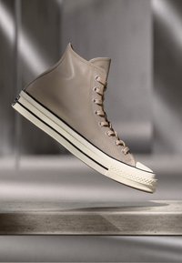 Beige Leder-Hochschuh mit runder Zehenpartie, weißer Gummisohle und schwarzem Streifen. Verfügt über acht Ösen und beigen Schnürsenkeln.