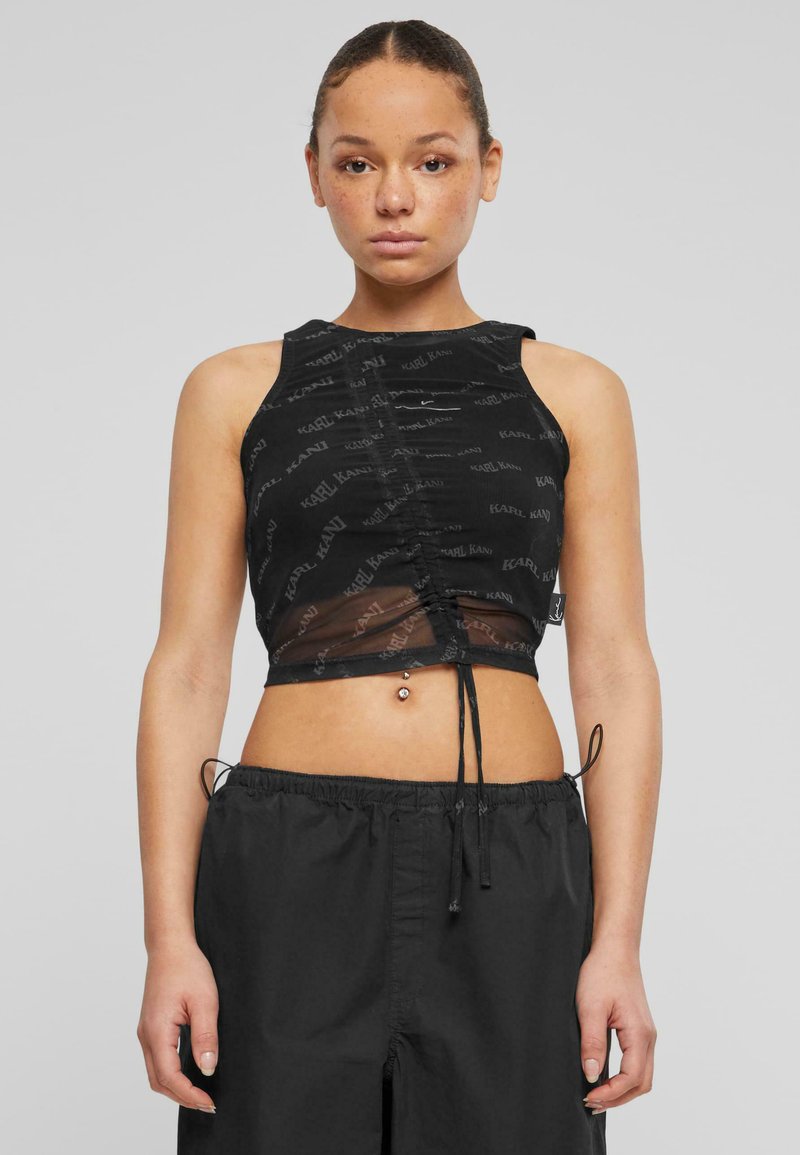 Svart crop top med en gjennomsiktig overlay, med et rynket design og gjentatt logo mønster. Knytes i bunnen og er uten ermer.