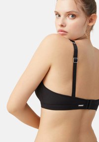 Sostén negro con tirantes ajustables, cierre rectangular en la parte posterior, textura suave, diseño simple y una etiqueta de marca sutil en la parte trasera.