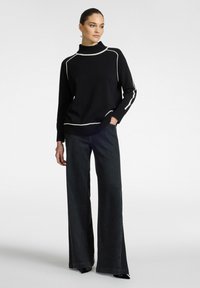 Maglione nero a collo alto con profili bianchi, vestibilità rilassata, orlo e polsini a costine, abbinato a jeans in denim scuro a gamba larga.