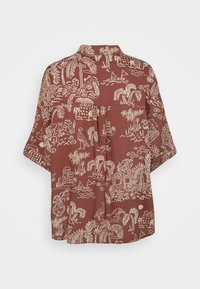 Chemise ample à manches courtes avec un fond marron et un imprimé tropical beige représentant des palmiers, des oiseaux, des bateaux et des bâtiments, vue de dos.