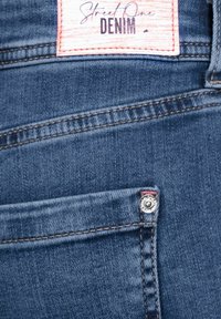 Tissu en denim bleu foncé avec une étiquette indiquant "Street One DENIM". Comprend un bouton en métal distinct et un détail de couture contrasté.