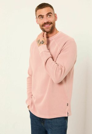 Hellrosa geripptes Sweatshirt mit Rundhalsausschnitt und langen Ärmeln, seitlichen Schlitzen und Logotag, kombiniert mit dunkelblauen Denim-Jeans.