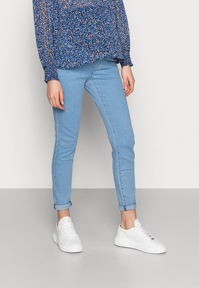 Ljusa blå skinny jeans med uppvikta nederkanter, matchade med vita sneakers. Jeansen är tillverkade av denim och har en slät textur.