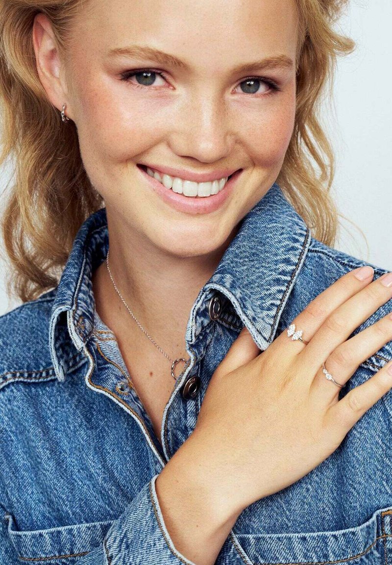 Silver smycken med en fjärilsdesign, bärs på en hand. Ett silverhalsband med en löpande hänge och en jeansjacka med knappdetaljer.