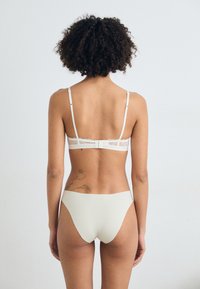 Set de lenjerie de culoare bej deschis, care include un sutien cu detalii din dantelă și bretele ajustabile, asociat cu chiloți înalți fără cusături, asortați.