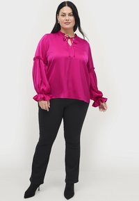Magenta satinbluse med en rynket krave, nøglehulshalsshalsudskæring og voluminøse ærmer, parret med sorte tætsiddende bukser og spidse sorte heels.