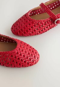 Piros fonott Mary Jane balerina kör alakú orral és ezüst csatpánttal világos háttéren.