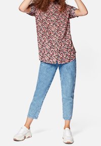 Camicetta a maniche corte floreale con sfondo nero, fiori rosa e bianchi; jeans azzurri chiari, leggermente svasati; sneakers bianche con dettagli beige.