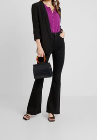 Svart kavaj, lila skjorta med knappar och svarta utsvängda byxor. Inkluderar en liten marinblå väska med ett orange handtag och svarta sandaletter med remmar.