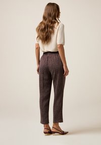 Crème, korte mouwen top gecombineerd met hooggewaist, bordeauxrode textuurbroek. Het model draagt donkere, gestrikte hakken en toont een casual outfit.