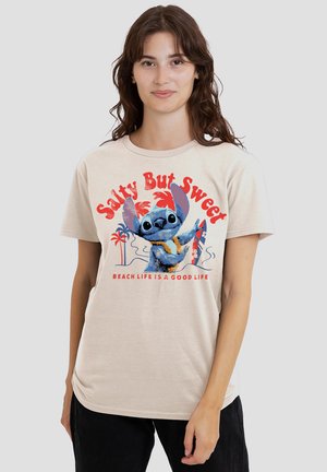 Beige cotton t-shirt featuring a graphic print of a character in blue with red and palm tree accents. Text reads "Salty But Sweet."