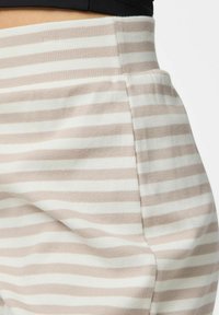 Prugaste hlače od teksturirane tkanine, s izmjeničnim svijetlo bež i bijelim prugama, srednje visoki pojas i detalj sa bočne strane.