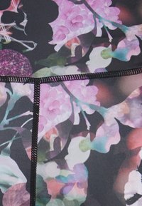 Färgglatt tyg med blommönster i rosa och gröna nyanser, mot en mörk bakgrund. Svart sömnad framhäver designen.