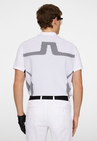 Vit, ribbad pikétröja med svarta vertikala ränder på baksidan. Korta ärmar, klassisk krage, kombinerad med vita byxor och svarta handskar.