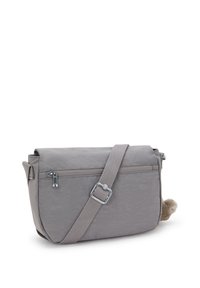 Bolso cruzado gris con correa ajustable, bolsillo con cremallera en la parte frontal y un pequeño llavero de peluche adjunto en el lado.