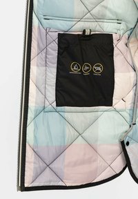Die Innenseite der gesteppte Jacke zeigt ein pastellfarbenes Karomuster. Sie verfügt über eine schwarze Tasche mit wasserabweisenden, winddichten und daunefreien Symbolen.