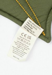 Grön tygkudde med gul söm. Skötselrådsetiketten innehåller tygsammansättning och tvättinstruktioner. Tillverkad i Indien.