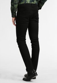 Black denim jeans with a slim fit, featuring back pockets and a smooth texture. Worn with a patterned green shirt and black shoes.