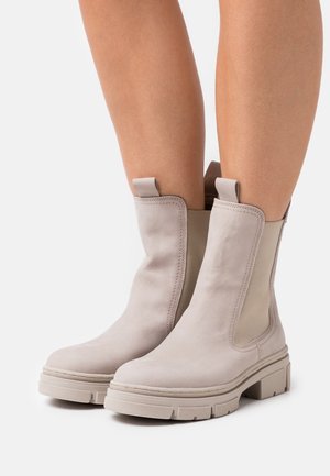 Bottines beiges claires en cuir souple, dotées de panneaux latéraux élastiques, d'un talon bloc et d'une semelle en caoutchouc texturée pour une meilleure adhérence.