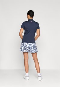 Marineblå polo skjorte med korte ærmer kombinert med et hvitt skjørt med et blått abstrakt mønster, båret med hvite sko og ankelstrømper.