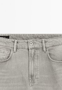 Jean en denim gris clair avec bouton à l'avant, passants de ceinture et poches avant visibles, présenté sur fond blanc.