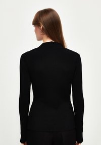 Zwarte geribbelde longsleeve top met een aansluitende pasvorm en een bescheiden halslijn. Zachte textuur en een gladde afwerking, met een sluiting aan de achterkant.