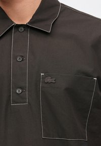 Σκοτεινό, πουκάμισο με κουμπιά και μυτερό γιακά. Διαθέτει αντίθετη λευκή ραφή και κεντημένο λογότυπο στην τσέπη του στήθους.