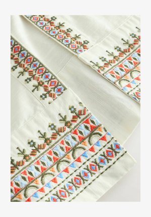 Broderad tyg med en krämfärgad bakgrund, intrikata mönster i röd, blå och grön, med texturerade detaljer på kanterna.