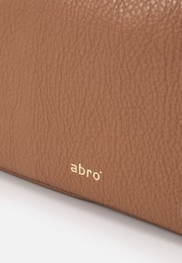 Hnědá kožená taška s текстurovaným povrchem; obsahuje zlaté logo "abro" v dolním rohu; jednoduchý obdélníkový tvar.