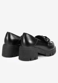 Zapatos de cuero negro con un tacón de plataforma grueso. Presentan un acabado suave y detalles decorativos en el empeine.
