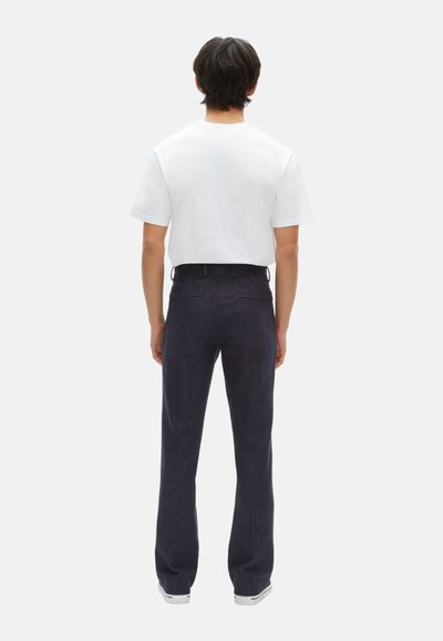 Witte T-shirt met korte mouwen in combinatie met donkerblauwe broeken. De broeken hebben een rechte snit, een lichte textuur en achterzakken.