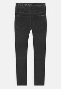Vaqueros negros de textura suave, con cintura de altura media, diseño de cinco bolsillos y cinturilla con marca de Calvin Klein.