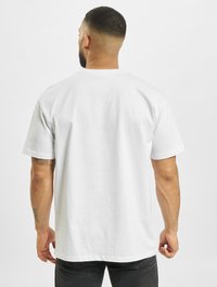 Hvit bomulls-T-skjorte, korte ermer, avslappet passform, rund hals, synlig søm. Brukt med mørke jeans. Enkel bakvisning, uten grafikk eller logoer.