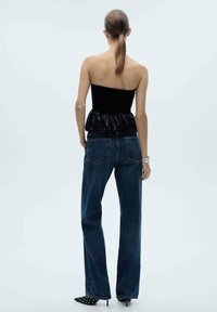 Top negro sin tirantes con un dobladillo con volantes, emparejado con jeans de mezclilla azul oscuro de cintura alta y tacones negros puntiagudos con puntos blancos.