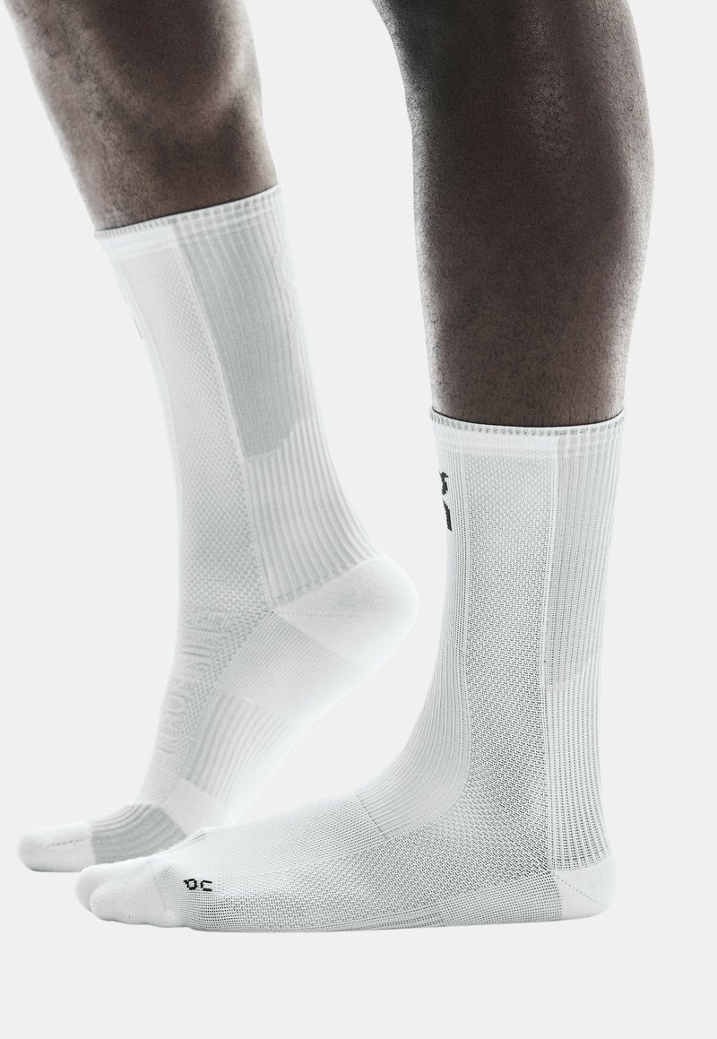 Calze sportive bianche con texture a costine e punta rinforzata. Presentano pannelli in rete per la traspirabilità e un logo sul lato.