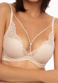 Koronkowy biustonosz w delikatnym odcieniu nude z głębokim dekoltem, regulowanymi ramiączkami oraz centralnym złotym akcentem. Posiada kwiatowy wzór i gładką fakturę.