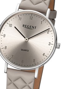 Montre à quartz avec un cadran rond argenté, un bracelet en cuir texturé gris clair et des index horaires noirs. Logo de la marque "REGENT" en haut.
