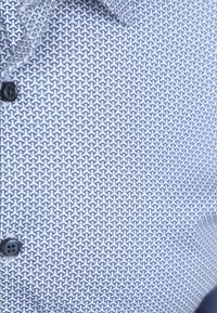 Korte mouwen shirt met een blauw-wit geometrisch patroon, voorzien van zwarte knopen en een gestructureerde stof.