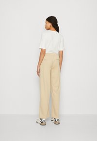 Light beige wide-leg pants with a soft texture, elastic waistband, and two back pockets; paired with a white short-sleeve top.