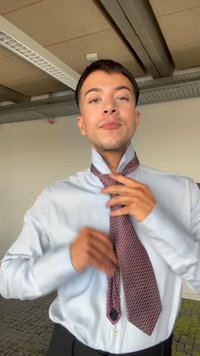 Eine Person in einem hellblauen Hemd richtet in einer Büroumgebung eine gemusterte rote Krawatte um den Hals.