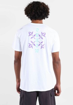 T-shirt blanc avec un motif graphique de feuilles violettes et aqua ainsi qu'un texte au dos. Manches courtes et coupe décontractée. Texture en coton lisse.