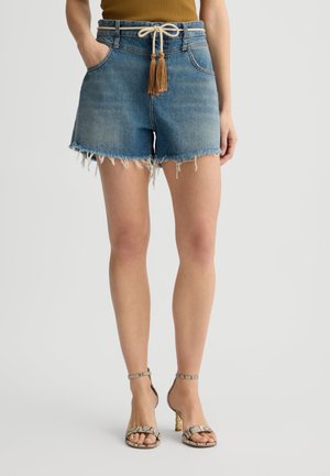 Shorts in denim con orlo sfilacciato, colore azzurro chiaro, e un laccio beige con pon-pon. Abbinati a tacchi con stampa serpente.