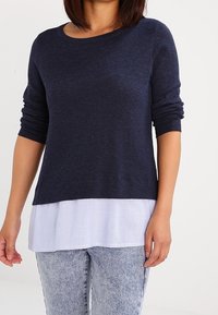 Navy blue sweater with long sleeves layered over a white and blue striped shirt. Soft texture and casual design with round neckline.