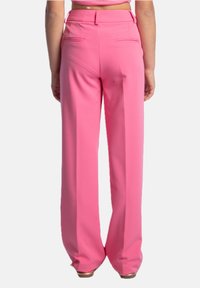 Pantaloni larghi rosa con una texture morbida. Presentano tasche posteriori e un design a vita alta, offrendo una vestibilità rilassata.