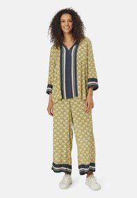 Completo giallo a fantasia con accenti blu navy, composto da una maglietta con scollatura a V e pantaloni larghi, realizzato in un tessuto leggero. Scarpe da ginnastica bianche casual.