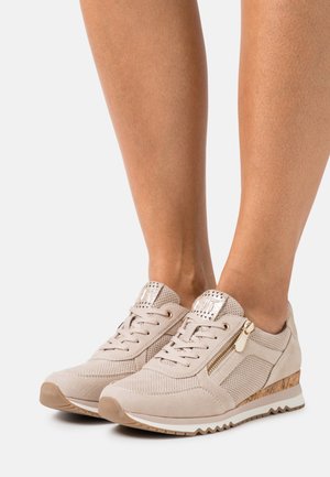 Beige damessneakers met geperforeerde details, veters aan de voorkant, gouden ritssluitingen aan de zijkant, sleehakken met kurkpatroon en witte rubberen zolen.