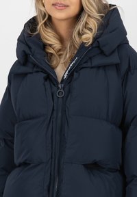 Giacca puffer blu navy con colletto alto, chiusura con zip e design a trapunta prominente. Presenta tasche laterali e una texture accogliente e imbottita.